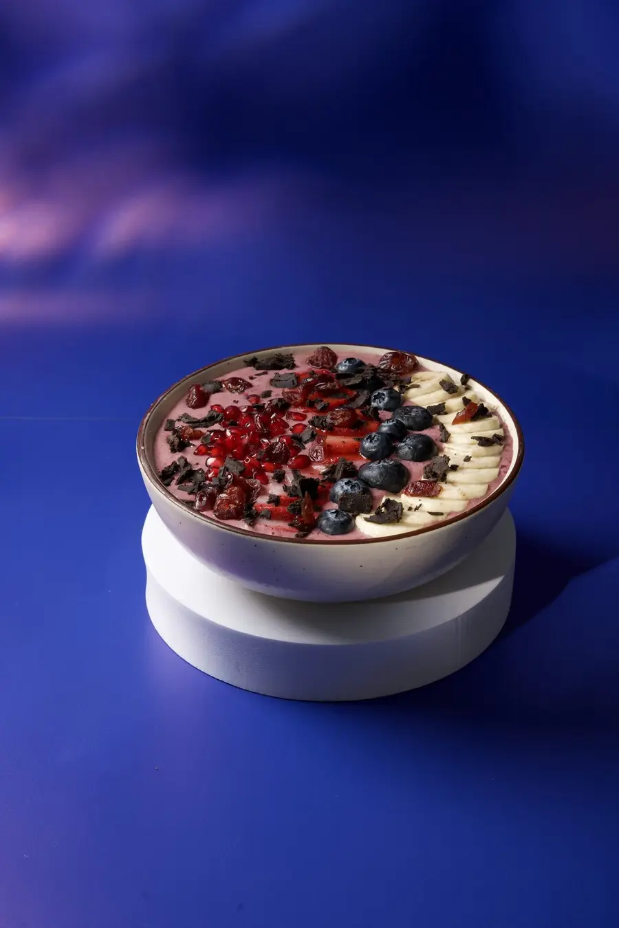 A berry bowl on a white plinth against a blue backdrop.